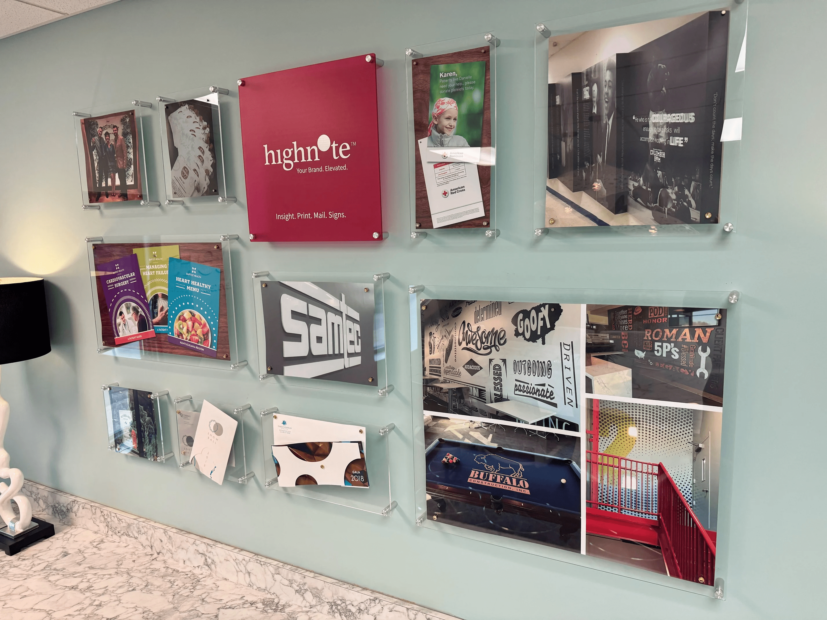 A wall display features a variety of framed posters and graphic design samples in a modern office setting, showcasing a company's work in branding, advertising, and design.