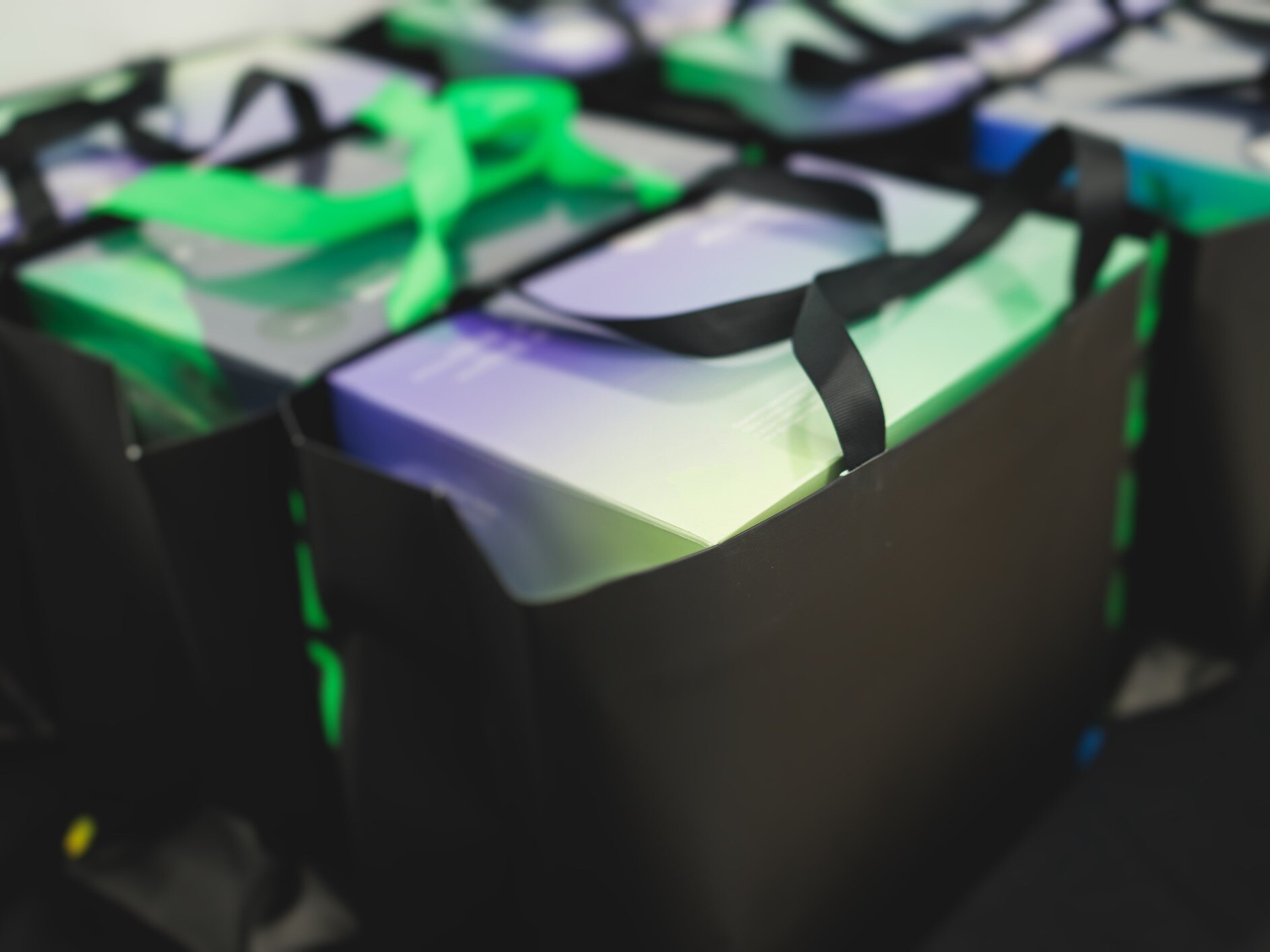 Black tote bags with gradient-colored boxes inside and a green ribbon handle.