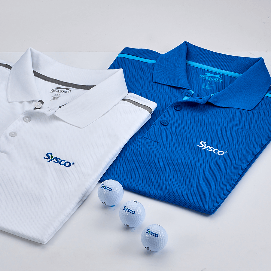 Two Sysco-branded polo shirts, one white and one blue, paired with three white golf balls featuring the Sysco logo, on a light background.